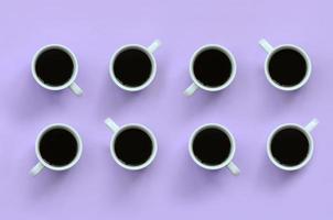 Many small white coffee cups on texture background of fashion pastel violet color paper in minimal concept photo