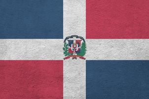 Dominican Republic flag depicted in bright paint colors on old relief plastering wall. Textured banner on rough background photo