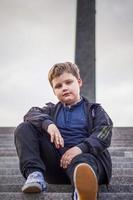 The boy is sitting on the steps in the open air against the background of skyscrapers and high-rise buildings. Journey. Lifestyle in the city. photo