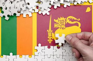 Sri Lanka flag is depicted on a table on which the human hand folds a puzzle of white color photo