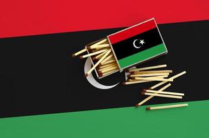 Libya flag is shown on an open matchbox, from which several matches fall and lies on a large flag photo