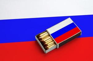 Russia flag is shown in an open matchbox, which is filled with matches and lies on a large flag photo