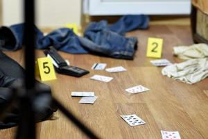 investigación de la escena del crimen - numeración de evidencias después del asesinato en el apartamento. un montón de naipes, billetera y ropa con marcadores de evidencia foto