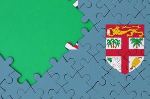 Fiji flag is depicted on a completed jigsaw puzzle with free green copy space on the left side photo