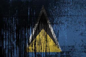 Saint Lucia flag depicted in paint colors on old and dirty oil barrel wall closeup. Textured banner on rough background photo