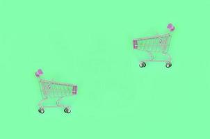 Shopping addiction, shopping lover or shopaholic concept. Small empty shopping cart lies on a pastel colored paper background. Flat lay minimal composition, top view photo