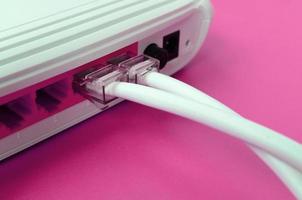 The Internet cable plugs are connected to the Internet router, which lies on a bright pink background. Items required for Internet photo