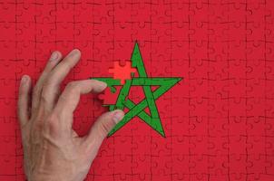 Morocco flag is depicted on a puzzle, which the man's hand completes to fold photo