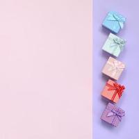 Small gift boxes of different colors with ribbons lies on a violet and pink color background photo