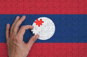 Laos flag is depicted on a puzzle, which the man's hand completes to fold photo