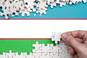 Uzbekistan flag is depicted on a table on which the human hand folds a puzzle of white color photo