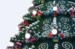 A fragment of a huge Christmas tree with many ornaments, gift boxes and luminous lamps. Photo of a decorated Christmas tree close-up with copy space