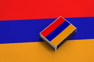 Armenia flag is pictured on a matchbox that lies on a large flag photo