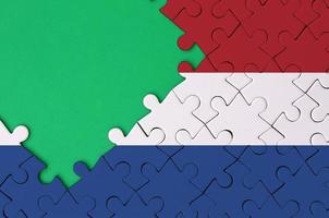 Netherlands flag is depicted on a completed jigsaw puzzle with free green copy space on the left side photo