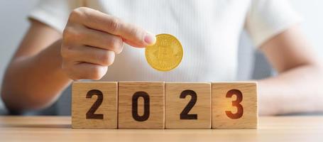 mano sosteniendo bitcoin dorado o criptomoneda btc en bloques de 2023 años. comercio criptográfico, es dinero digital, blockchain y conceptos de año nuevo foto