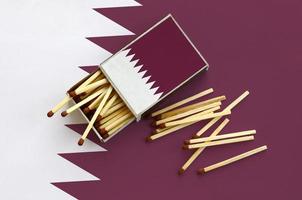 Qatar flag is shown on an open matchbox, from which several matches fall and lies on a large flag photo