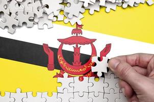 Brunei Darussalam flag is depicted on a table on which the human hand folds a puzzle of white color photo