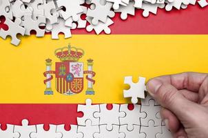 Spain flag is depicted on a table on which the human hand folds a puzzle of white color photo