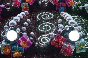 A fragment of a huge Christmas tree with many ornaments, gift boxes and luminous lamps. Photo of a decorated Christmas tree close-up