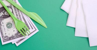 Disposable plastic cutlery green. Plastic fork and knife lie on a small amount of US dollars next to napkins photo