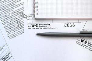 el bolígrafo y el cuaderno en el formulario de impuestos w-2 declaración de salarios e impuestos. la hora de pagar impuestos foto