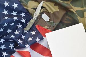 el papel en blanco se encuentra con un cuchillo y un collar de etiqueta de perro del ejército en uniforme de camuflaje y bandera estadounidense foto