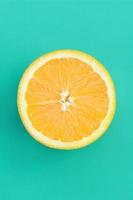 Top view of a one orange fruit slice on bright background in turquoise green color. A saturated citrus texture image