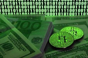 Two bitcoins lies on a pile of dollar bills on the background of a monitor depicting a binary code of bright green zeros and one units on a black background. Low key lighting photo