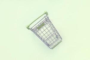Small shopping cart lies on a lime background. Minimalism flat lay photo