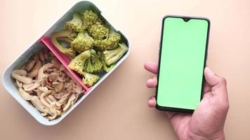 Person holds a smart phone with green screen next to a bento box lunch video