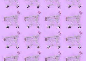 Shopping addiction, shopping lover or shopaholic concept. Many small empty shopping carts perform a pattern on a pastel colored paper background. Flat lay composition, top view photo