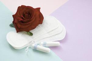 Menstrual pads and tampons with red rose flower on multicolored background photo