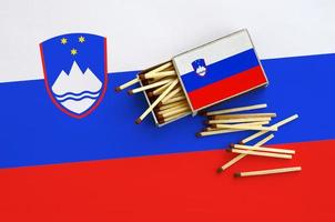 Slovenia flag is shown on an open matchbox, from which several matches fall and lies on a large flag photo