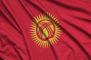 Kyrgyzstan flag is depicted on a sports cloth fabric with many folds. Sport team banner photo