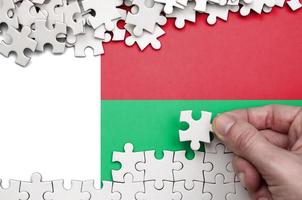 Madagascar flag is depicted on a table on which the human hand folds a puzzle of white color photo