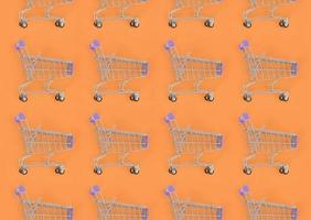 Shopping addiction, shopping lover or shopaholic concept. Many small empty shopping carts perform a pattern on a pastel colored paper background. Flat lay composition, top view photo