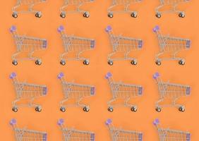 Shopping addiction, shopping lover or shopaholic concept. Many small empty shopping carts perform a pattern on a pastel colored paper background. Flat lay composition, top view photo