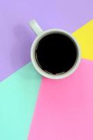 Small white coffee cup on texture background of fashion pastel blue, yellow, violet and pink colors paper in minimal concept photo