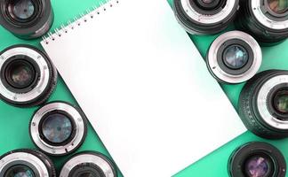 Several photographic lenses and white notebook lie on a bright turquoise background. Copy space photo