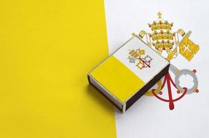 Vatican City State flag is pictured on a matchbox that lies on a large flag photo