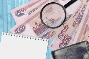 500 russian rubles bills and magnifying glass with black purse and notepad. Concept of counterfeit money. Search for differences in details on money bills to detect fake photo
