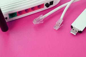 el enrutador de Internet, el adaptador wi-fi usb portátil y los enchufes de cable de Internet se encuentran sobre un fondo rosa brillante. elementos necesarios para internet foto