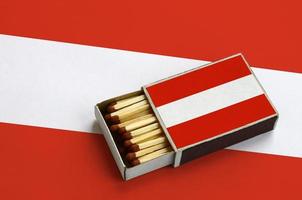 Austria flag is shown in an open matchbox, which is filled with matches and lies on a large flag photo