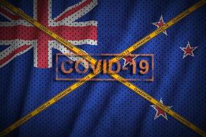 New Zealand flag and Covid-19 stamp with orange quarantine border tape cross. Coronavirus or 2019-nCov virus concept photo