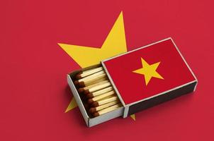 Vietnam flag is shown in an open matchbox, which is filled with matches and lies on a large flag photo