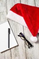fondo de navidad y año nuevo con sombrero rojo de santa, gafas, bloc de notas y bolígrafo para tus deseos