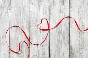 Feliz día de San Valentín. corazón de cinta roja sobre fondo blanco de madera foto