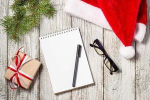 Christmas and Business Items with Copy Space cropped Santa Cap Notepad Pen Glasses and decorated Gift Box and fir tree photo