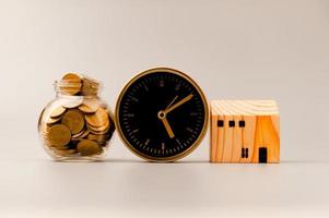 Golden alarm clock, model wooden house and silver gray background, coin saving ideas to build a home and personal business for a sustainable future. photo