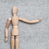 Small wooden figurine stretches out its hand and points to something against a gray felt background. Copy space. Top view. photo